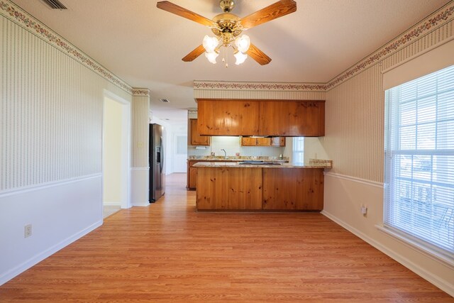 kitchen featuring wallpapered walls, a peninsula, light wood-style floors, stainless steel refrigerator with ice dispenser, and brown cabinets