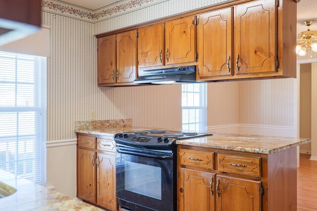 kitchen featuring wallpapered walls, black / electric stove, brown cabinetry, and under cabinet range hood