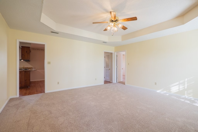 carpeted empty room with a tray ceiling, baseboards, visible vents, and ceiling fan