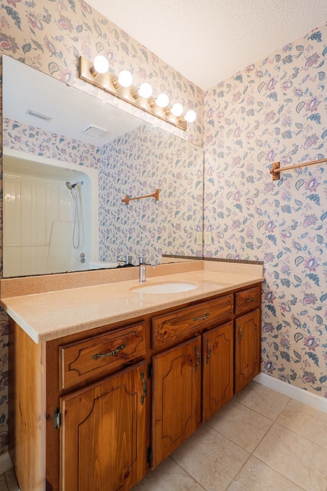 full bath with wallpapered walls, a textured ceiling, tile patterned flooring, baseboards, and vanity