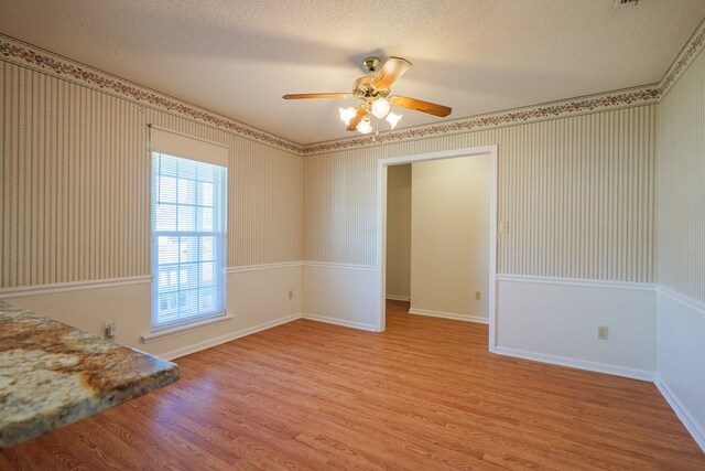 empty room with wallpapered walls, light wood-style floors, baseboards, and a textured ceiling