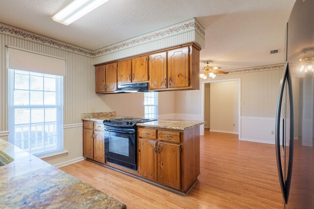 kitchen featuring wallpapered walls, freestanding refrigerator, exhaust hood, black electric range oven, and a textured ceiling