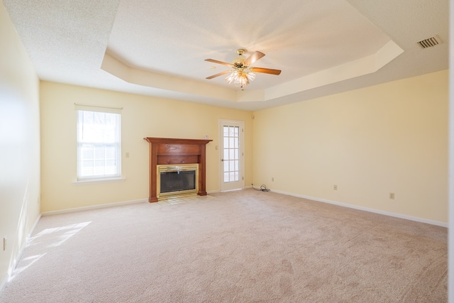 unfurnished living room with a tray ceiling, a fireplace with flush hearth, a healthy amount of sunlight, and visible vents