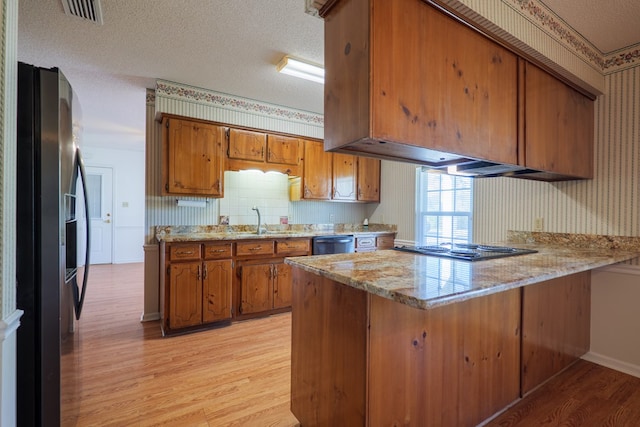 kitchen with wallpapered walls, a peninsula, brown cabinets, and appliances with stainless steel finishes