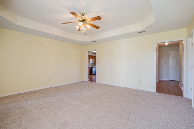 carpeted spare room with a tray ceiling, baseboards, visible vents, and ceiling fan