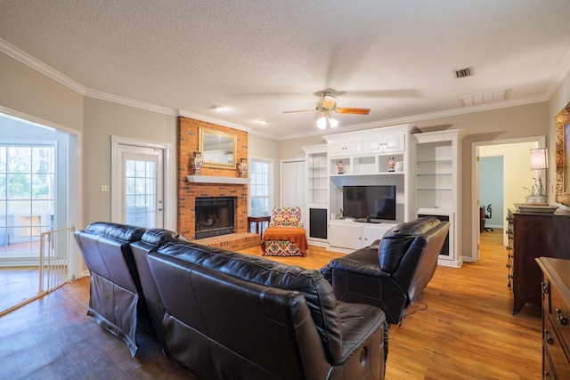 living room featuring a brick fireplace, ceiling fan, ornamental molding, a textured ceiling, and wood-type flooring