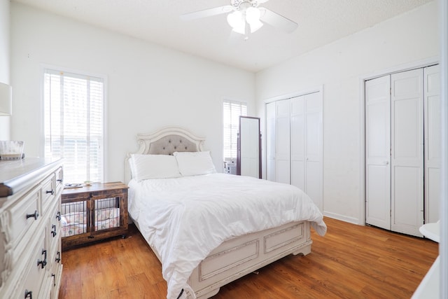 bedroom with ceiling fan, light wood-type flooring, a textured ceiling, and multiple closets