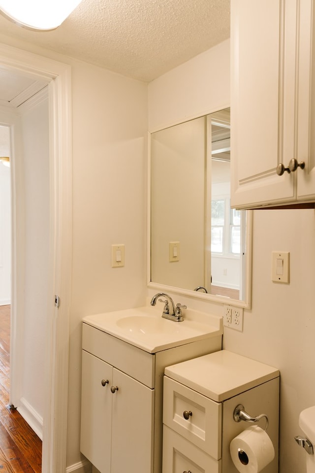 half bath featuring toilet, wood finished floors, a textured ceiling, and vanity