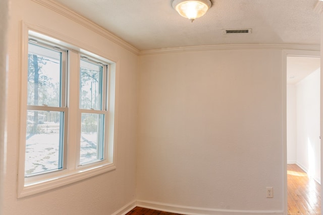 unfurnished room with baseboards, visible vents, wood finished floors, crown molding, and a textured ceiling