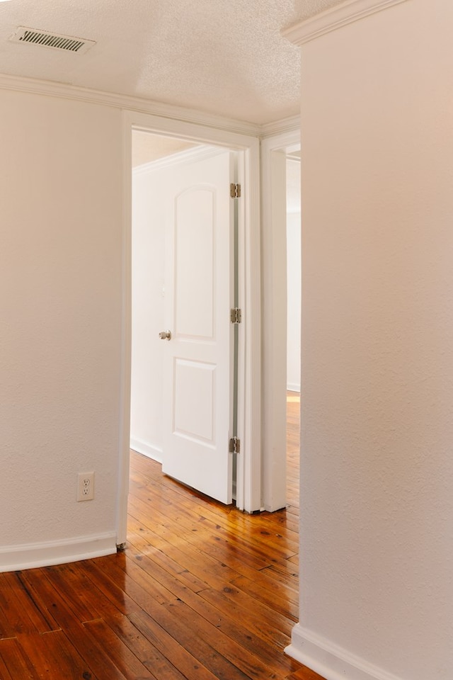 empty room featuring ornamental molding, visible vents, a textured ceiling, and wood finished floors