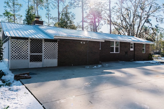 rear view of house featuring brick siding, a chimney, metal roof, a carport, and driveway