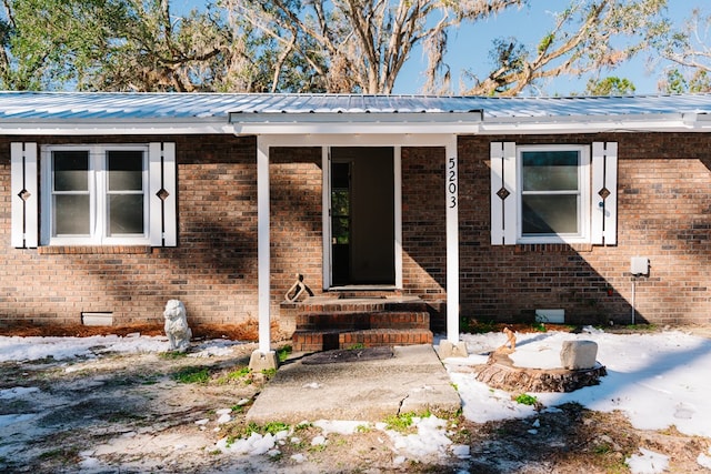 doorway to property featuring a patio area, crawl space, brick siding, and metal roof