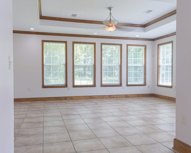 tiled empty room featuring ornamental molding and a tray ceiling