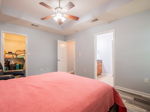 bedroom with baseboards, visible vents, a tray ceiling, and wood finished floors