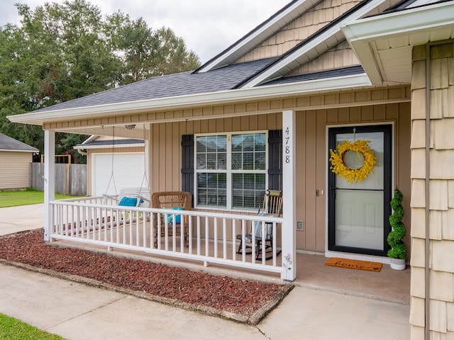 entrance to property with a shingled roof, covered porch, driveway, and an attached garage