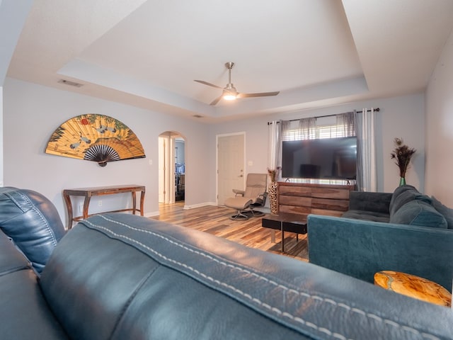 living area featuring arched walkways, a raised ceiling, visible vents, a ceiling fan, and wood finished floors