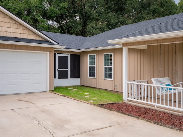 view of exterior entry with a garage, driveway, and roof with shingles