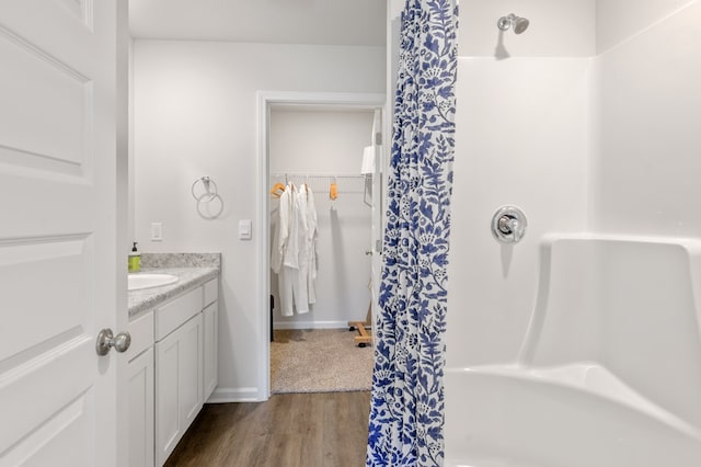 bathroom with curtained shower, a spacious closet, vanity, wood finished floors, and baseboards