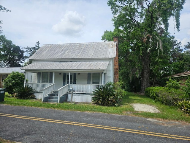 view of front facade featuring a chimney, covered porch, and metal roof