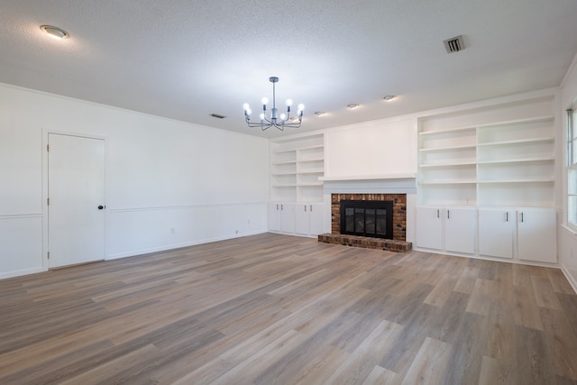 unfurnished living room featuring a brick fireplace, built in features, a chandelier, light hardwood / wood-style floors, and a textured ceiling