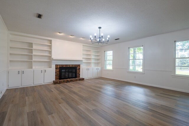 unfurnished living room featuring a notable chandelier, hardwood / wood-style floors, a textured ceiling, and a brick fireplace