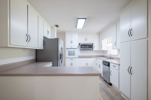 kitchen featuring kitchen peninsula, appliances with stainless steel finishes, sink, light hardwood / wood-style flooring, and white cabinets