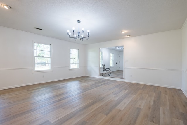 unfurnished room featuring a chandelier, a textured ceiling, and light hardwood / wood-style flooring