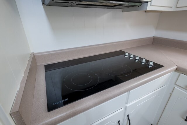 details with white cabinets, ventilation hood, and black stovetop