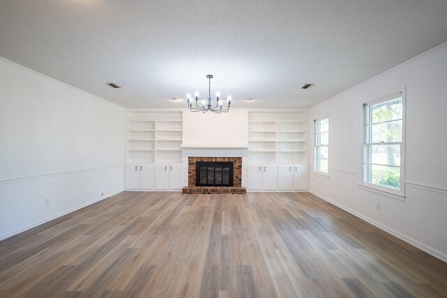 unfurnished living room featuring an inviting chandelier, ornamental molding, a textured ceiling, a fireplace, and wood-type flooring