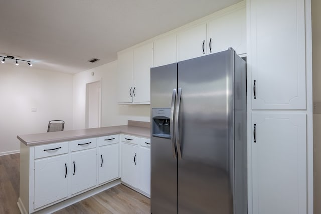 kitchen with kitchen peninsula, stainless steel fridge, white cabinets, and light hardwood / wood-style flooring