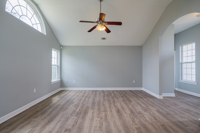 empty room featuring a ceiling fan, arched walkways, baseboards, and wood finished floors