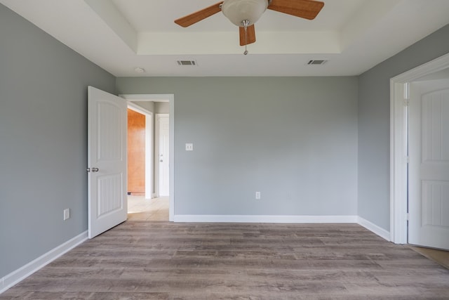 unfurnished bedroom with a tray ceiling, wood finished floors, visible vents, and baseboards