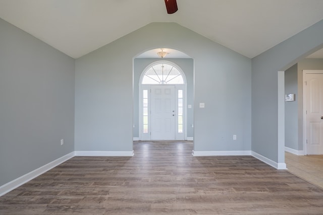 foyer entrance with arched walkways, vaulted ceiling, baseboards, and wood finished floors