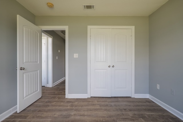 unfurnished bedroom with dark wood-type flooring, a closet, visible vents, and baseboards