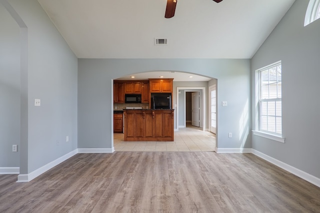 unfurnished living room featuring baseboards, visible vents, arched walkways, vaulted ceiling, and light wood-type flooring