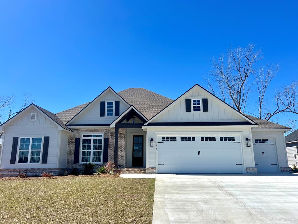 craftsman-style home featuring brick siding, concrete driveway, board and batten siding, a garage, and a front lawn