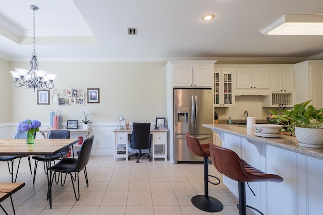 kitchen featuring stainless steel refrigerator with ice dispenser, hanging light fixtures, ornamental molding, a notable chandelier, and light stone counters