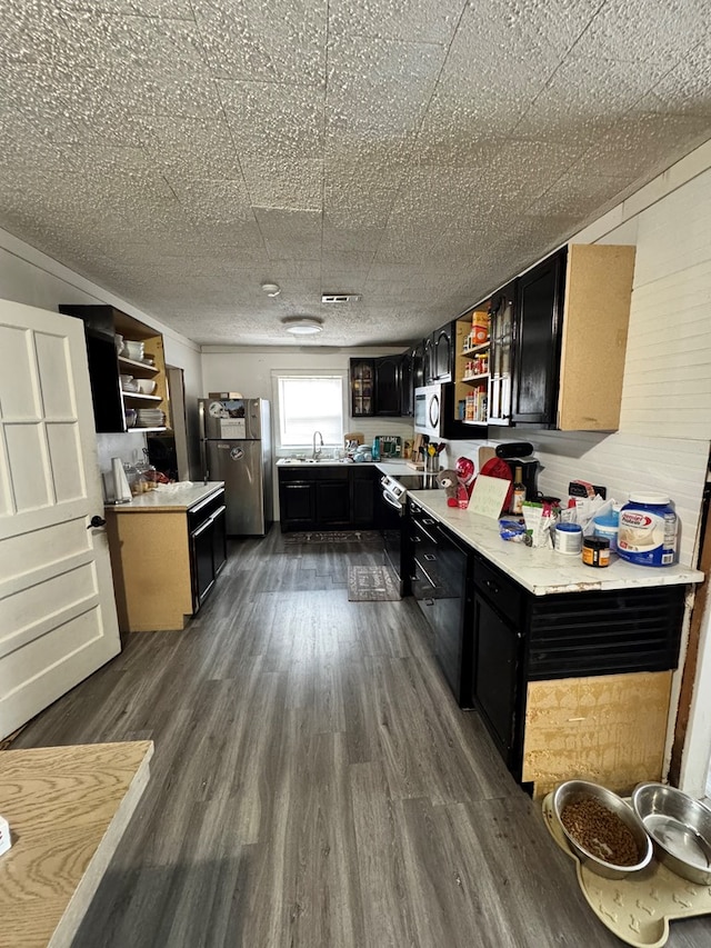 kitchen with open shelves, stainless steel appliances, dark cabinetry, light countertops, and dark wood-style flooring