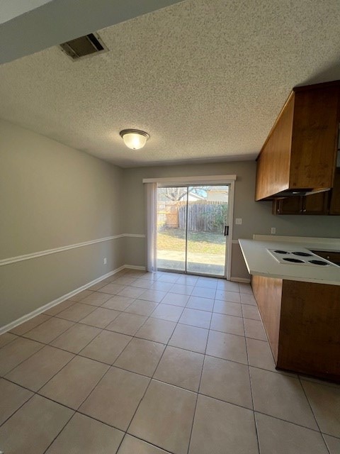 kitchen with premium range hood, white electric cooktop, light tile patterned floors, and a textured ceiling