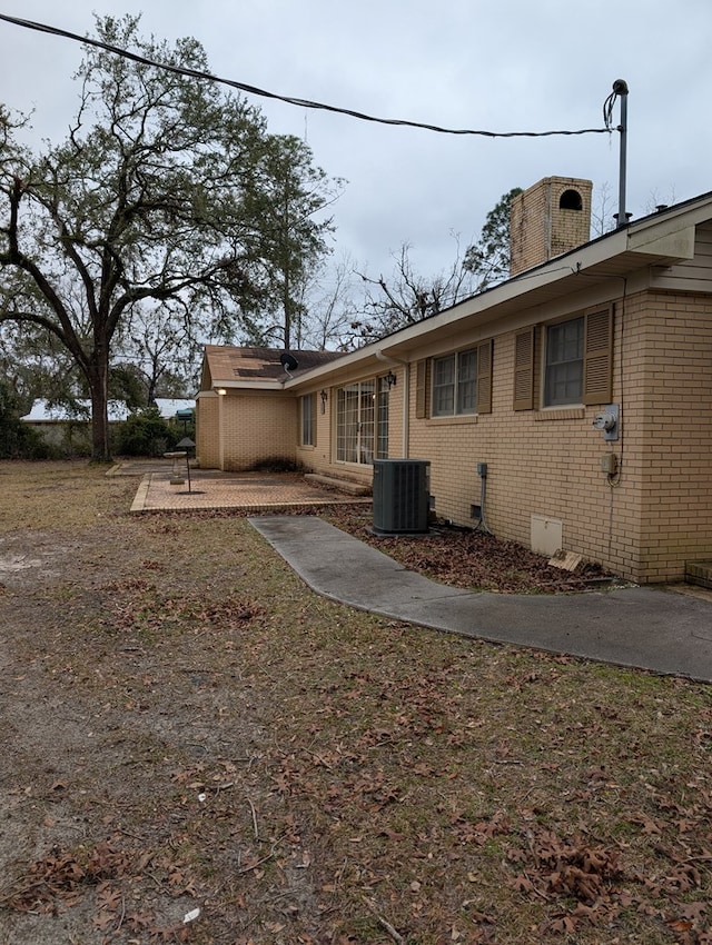 view of side of home with crawl space, brick siding, a chimney, and cooling unit