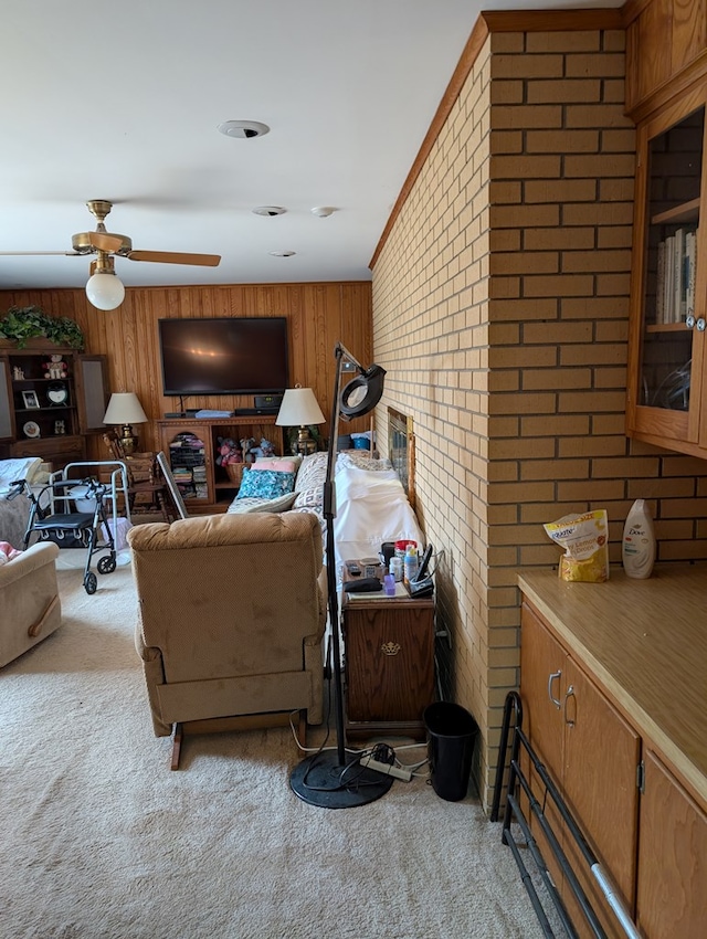 living area with brick wall, wood walls, a ceiling fan, and light colored carpet