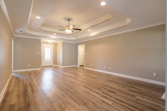 empty room with ceiling fan, light hardwood / wood-style floors, a raised ceiling, and ornamental molding