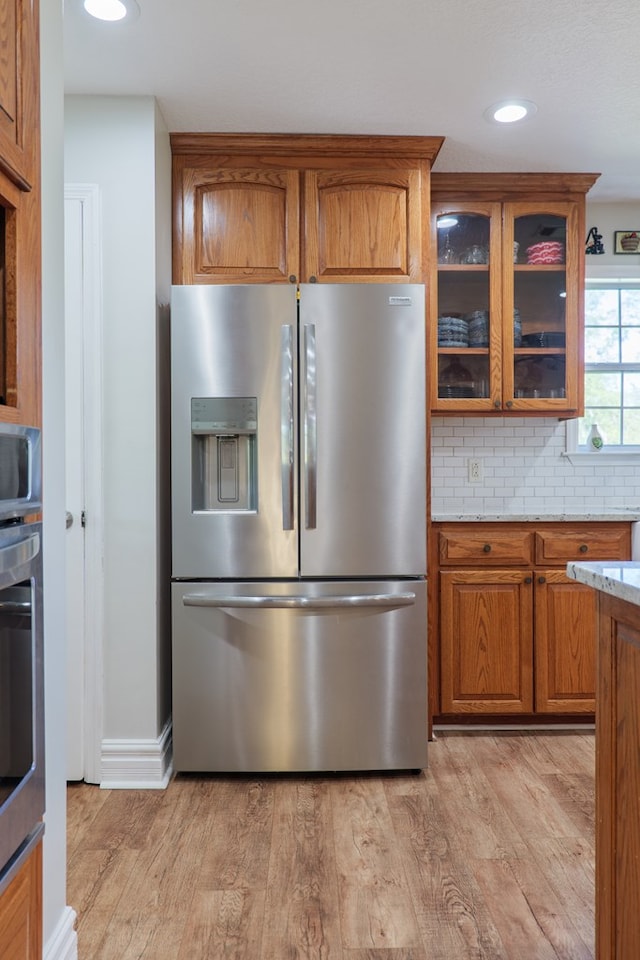 kitchen featuring brown cabinetry, light wood-style floors, appliances with stainless steel finishes, and backsplash
