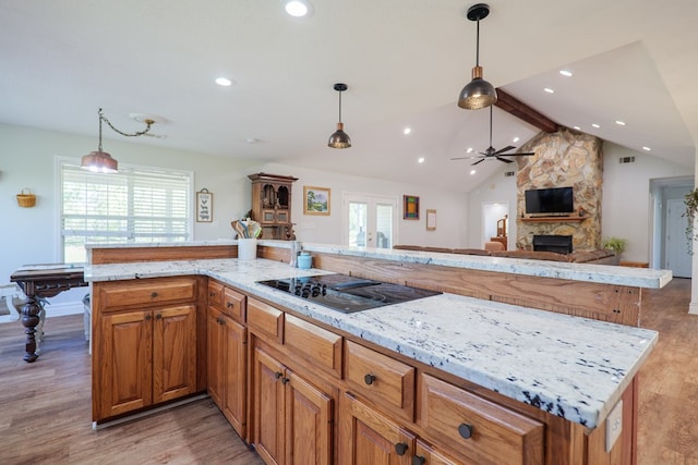 kitchen featuring lofted ceiling with beams, a stone fireplace, a ceiling fan, light wood-style floors, and black electric stovetop