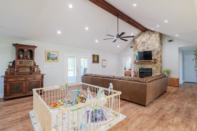 living room featuring light wood-type flooring, a stone fireplace, visible vents, ceiling fan, and vaulted ceiling with beams