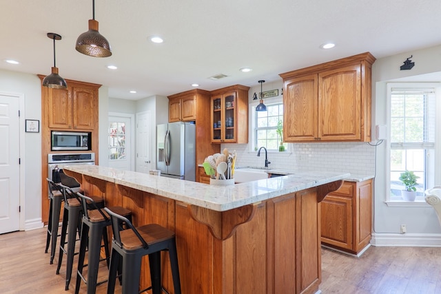 kitchen with glass insert cabinets, light stone countertops, appliances with stainless steel finishes, light wood finished floors, and decorative backsplash