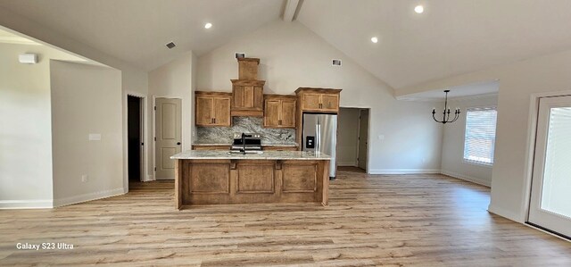 kitchen with a chandelier, light wood-type flooring, appliances with stainless steel finishes, a kitchen island with sink, and decorative backsplash