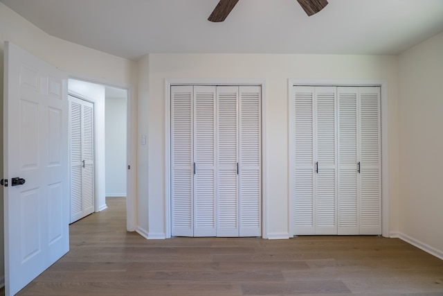 unfurnished bedroom featuring baseboards, a ceiling fan, multiple closets, and wood finished floors