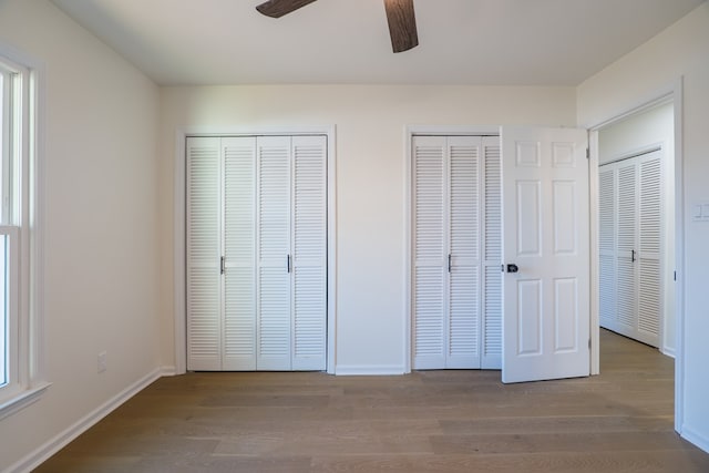 unfurnished bedroom featuring baseboards, multiple closets, wood finished floors, and a ceiling fan