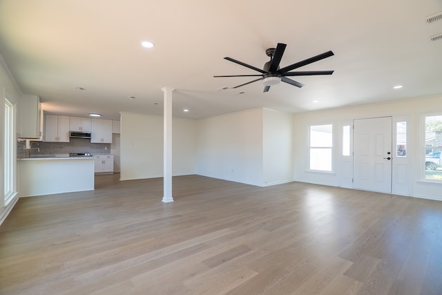 unfurnished living room featuring a ceiling fan, a sink, recessed lighting, light wood-style floors, and ornate columns